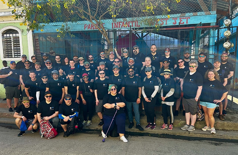 team-photo-dominican-retreat Group photo of Bursting Silver team members in matching black shirts, gathered outside a colorful building, showcasing teamwork and community engagement during a Dominican Republic retreat.